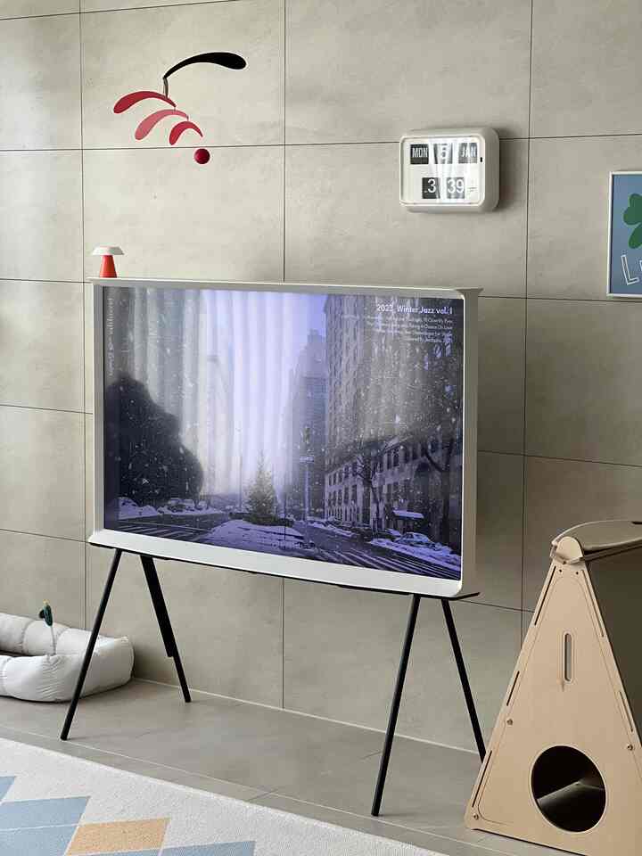 ベージュのタイル壁と自然素材のキャットハウスがあるモダンなリビング、サムスンザセリフテレビとキャットスクラッチャーが配置された居心地の良いペット対応空間