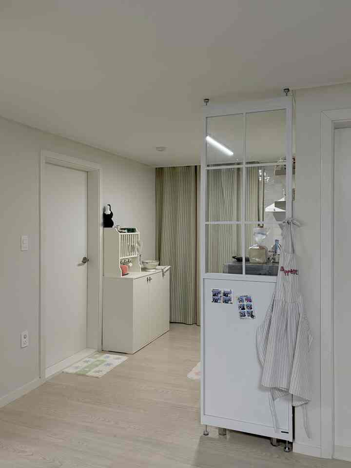 柔らかい白とベージュのトーンのキッチン空間、鉄製パーティションとエプロンが配置された印象的なインテリア