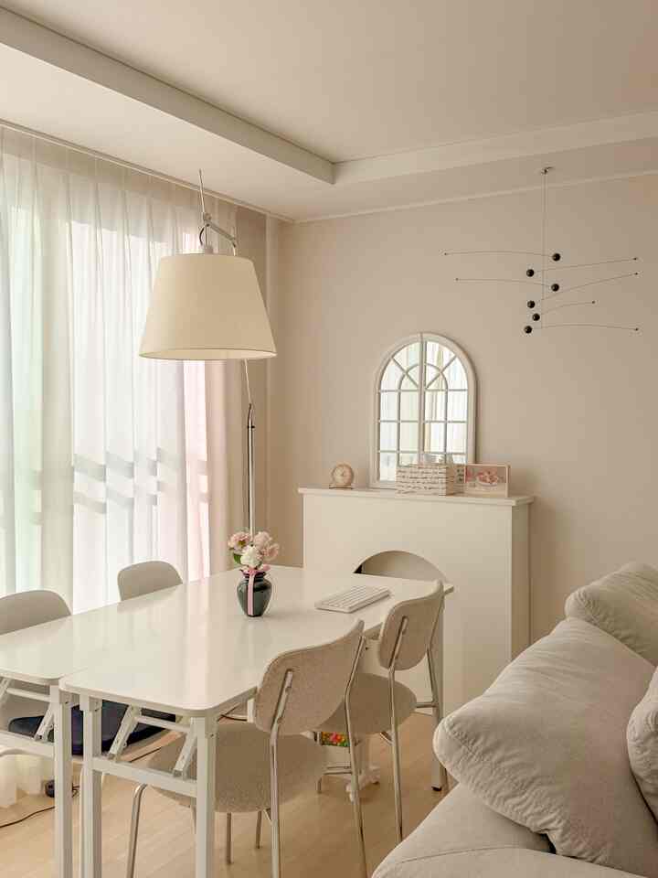 明るいホワイトとナチュラルな色調のリビングルーム、シンプルなデスクと椅子、ソファが配置された落ち着いた雰囲気のインテリア