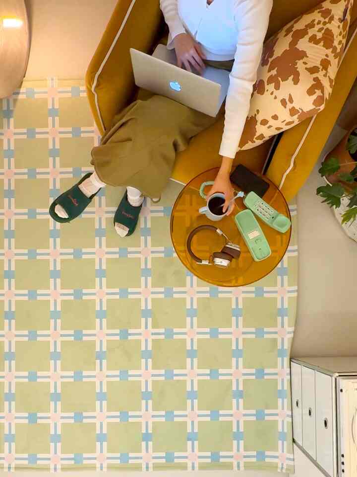 黄色と茶色のトーンのリビング、黄色のソファと茶色の柄クッション、チェッカーパターンのラグが配置された雰囲気のあるホームオフィス