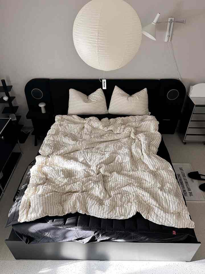 モノトーンの寝室、中央に黒いベッドフレームと淡いストライプの寝具が配置されたモダンで清潔感のあるインテリア