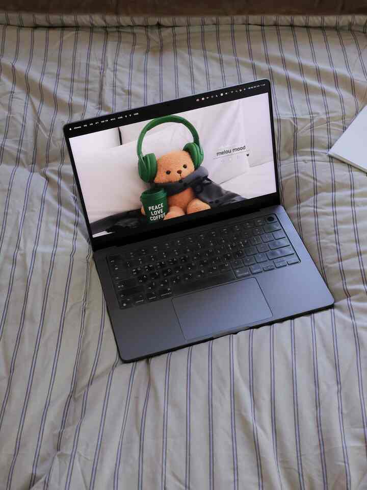 白い寝具と緑のアクセントが配置された寝室、ベッドの上のノートパソコンが印象的な空間