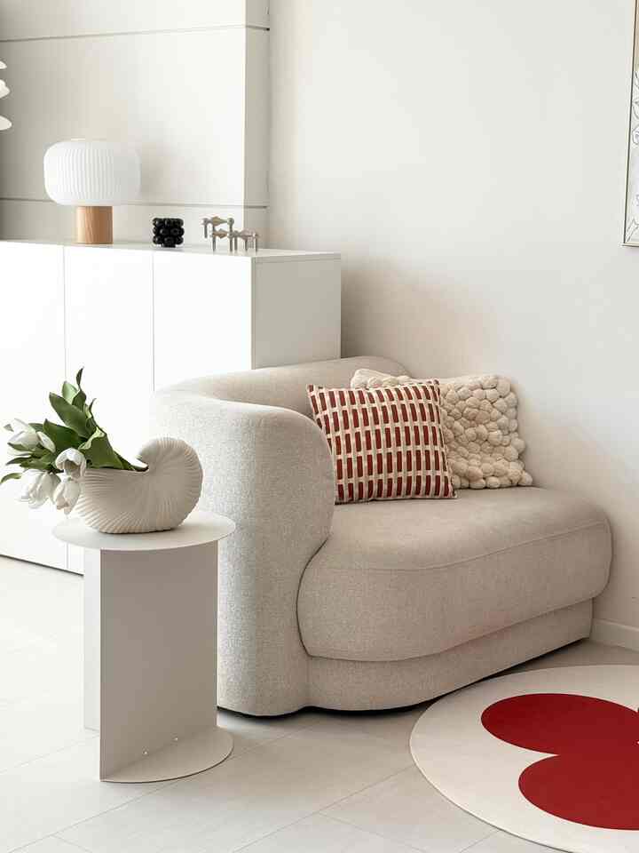 ホワイトとベージュのトーンの玄関空間、曲線のソファとサイドテーブル、赤いアクセントラグが調和した落ち着いた雰囲気のインテリア