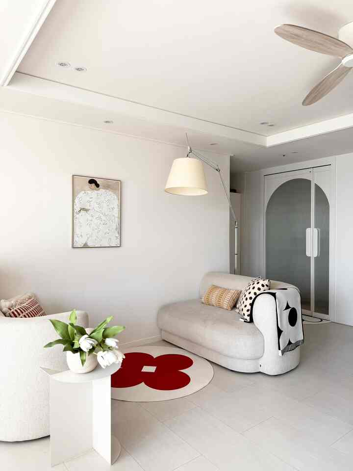 白とベージュの色調のリビング、モジュラーソファと赤い花柄の丸いラグ、花瓶と照明が配置された清潔感のあるモダンなインテリア