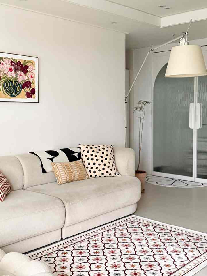 ベージュとホワイトの色調のリビング、ベージュのソファとパターンカーペット、フロアランプが配置されたシンプルで自然な雰囲気のインテリア