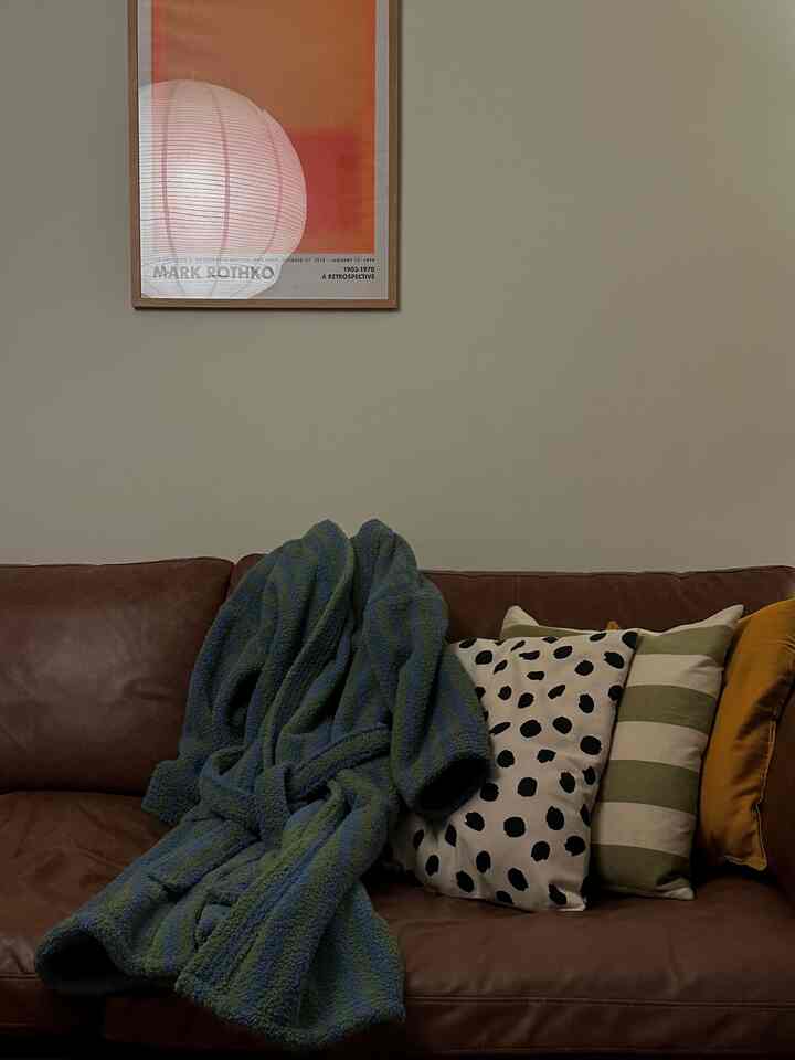 Beige-toned wall with brown leather sofa, assorted cushions, and throw blanket in cozy living room interior