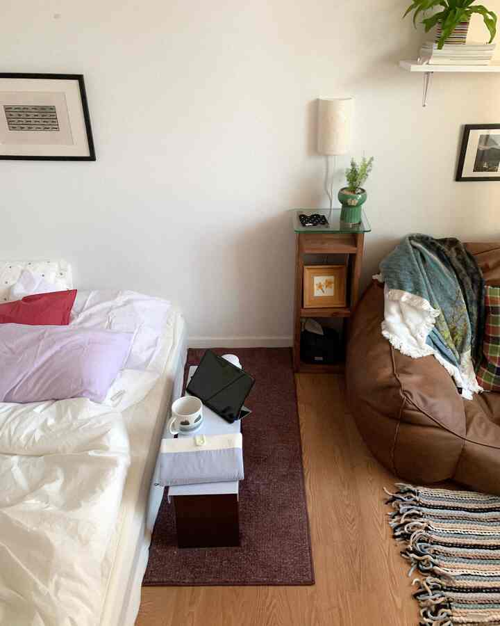 白い壁とブラウンの家具が調和する寝室、ベッド横に小さなサイドテーブルとビーンバッグソファが配置された落ち着いた空間