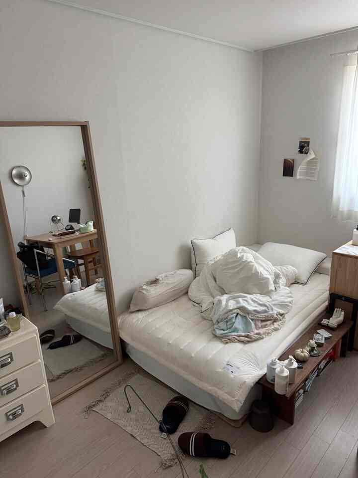 白を基調にウッドトーン家具が調和するナチュラルでシンプルな寝室、マットレスや全身鏡、小さなチェストが見える