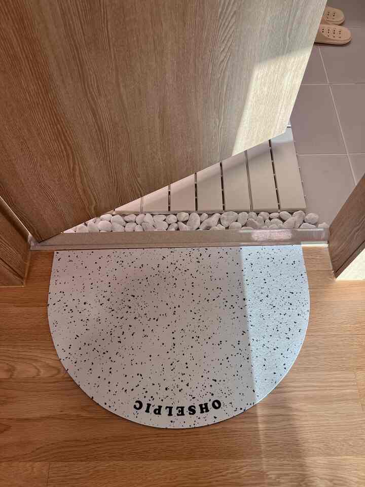 木目調とホワイトの浴室入口、半円形の白い斑点模様のバスマットと木製のドアと床が配置された清潔感のある空間