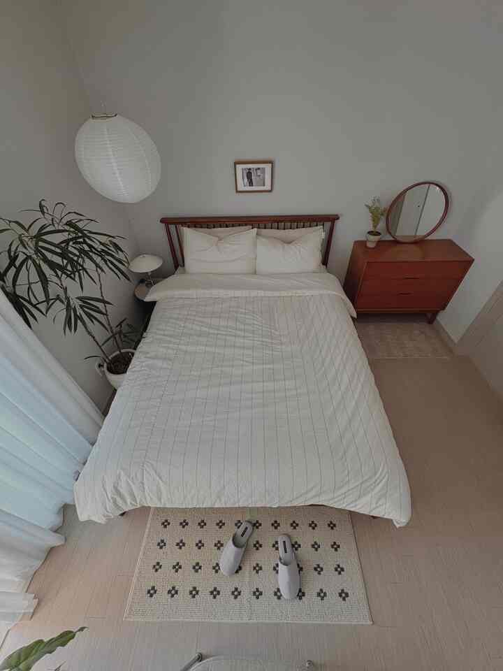 Minimal bedroom with wood tone and white hues, featuring a bed, vanity, plant, and a cozy atmosphere