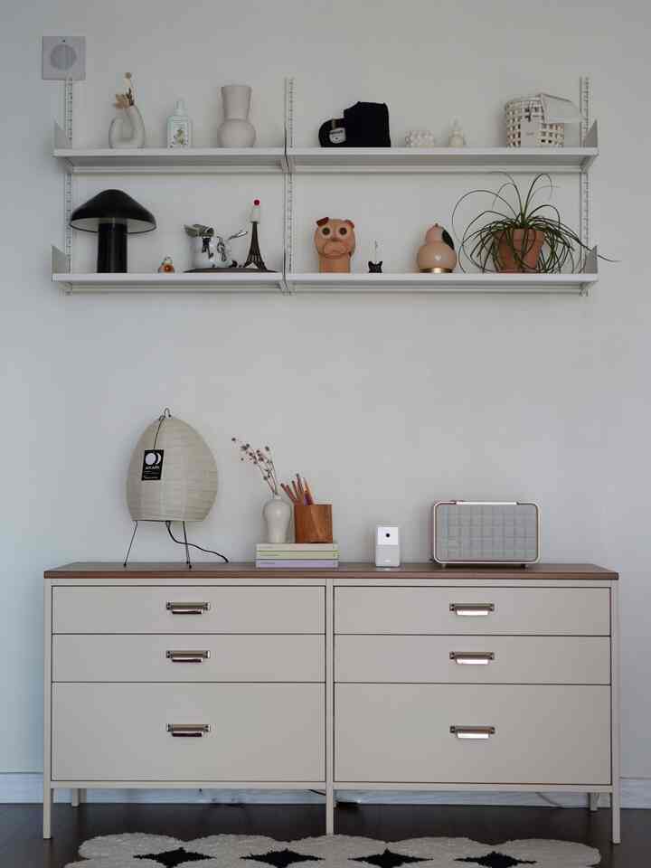 白い壁とナチュラルな色調のチェストがある空間、棚に様々なオブジェが配置された印象的なインテリア