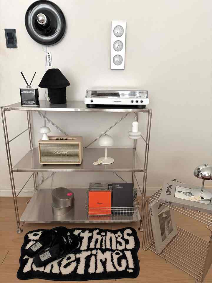 白い壁と木目調の床、メタルシェルフにオーディオ機器と照明が配置されたミニマルなリビングスペース