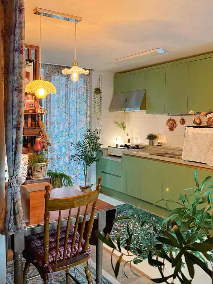 グリーントーンが際立つヴィンテージ風キッチン、木製ダイニングテーブルと豊かな植物が調和する居心地の良い空間