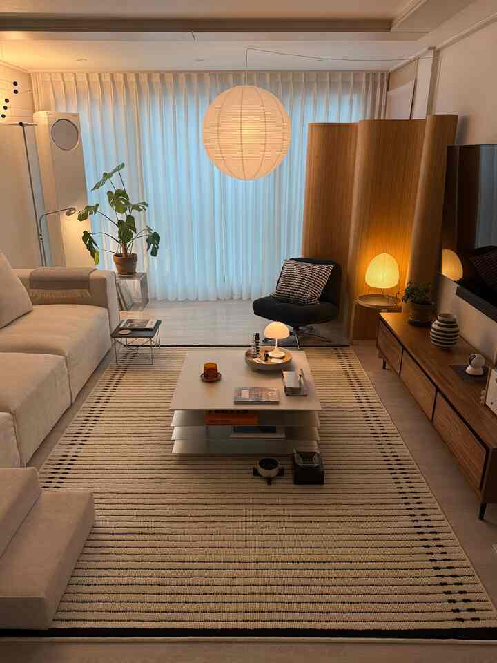 ナチュラルな木目調と白いカーテンのリビング、ベージュのラグとモダンな家具が配置された雰囲気のあるインテリア