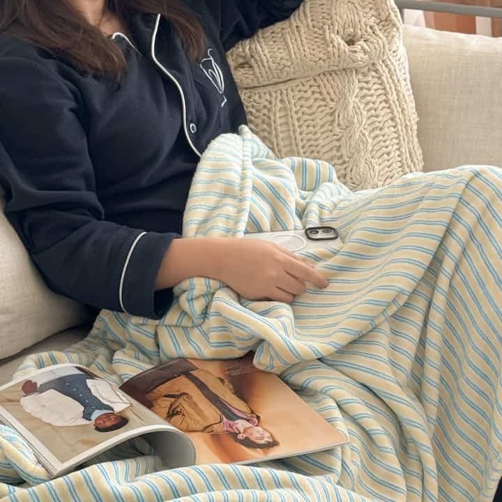 柔らかなベージュのソファにパステルブルーのストライプブランケットが掛けられた居心地の良いリビング