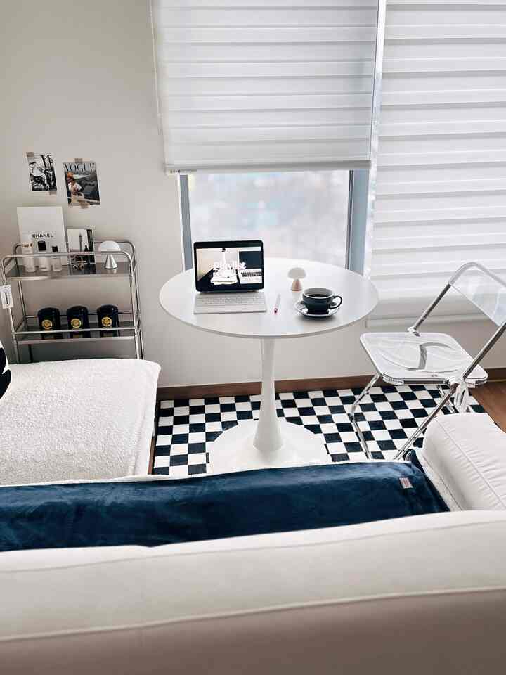 モノトーンのミッドセンチュリーモダンリビング、透明な椅子と丸いテーブル、チェッカーボードラグが配置されたシンプルな空間