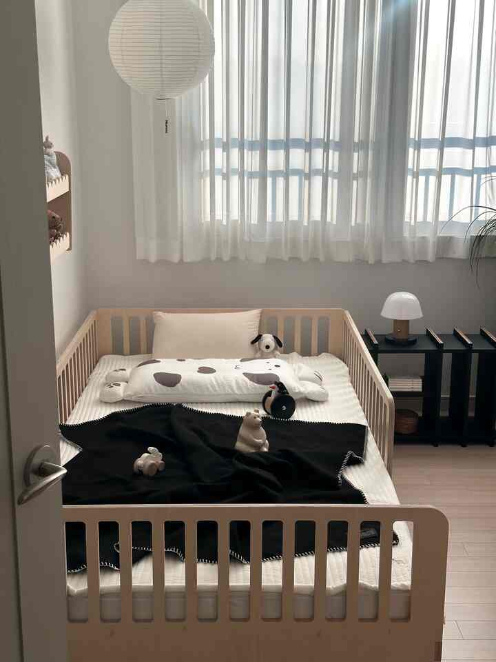 白とナチュラルカラーのベビールーム、ベビーベッドとスロー、大きな枕が配置された清潔感と温かみのあるインテリア