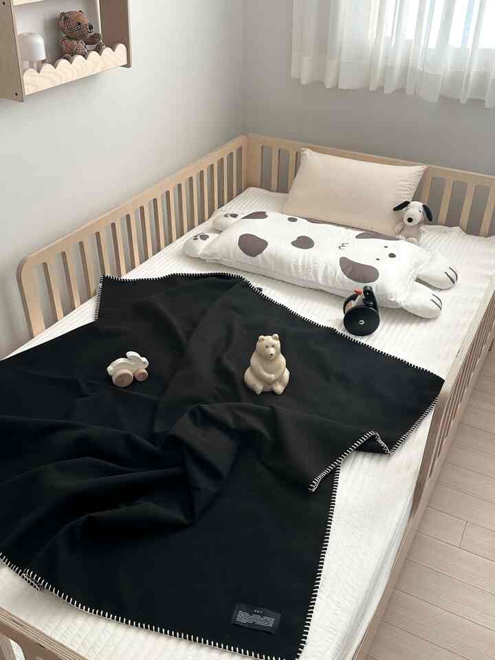 白とナチュラルカラーの幼児用寝室、木製ベッドと黒いブランケット、かわいいおもちゃが配置された雰囲気のある空間