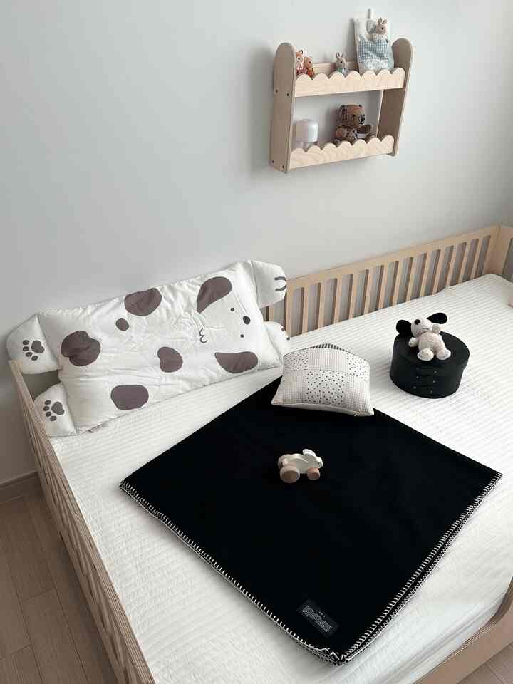 白とナチュラルな色調の子供部屋、ベビーベッドと黒いブランケット、かわいいおもちゃが置かれた雰囲気のある空間
