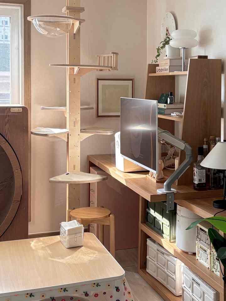 ナチュラルな木目調とベージュが調和したリビング兼ホームオフィス、大型キャットタワーとモニターが見える整った空間