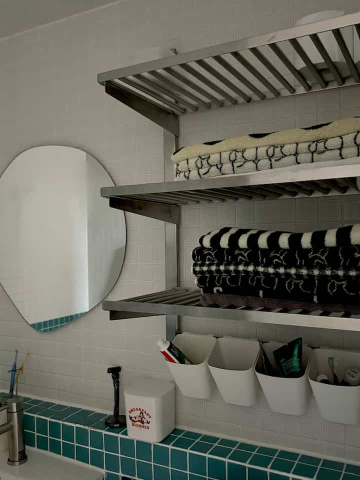 白と黒のトーンのバスルーム、金属製の棚にタオルと用品が配置された清潔感のあるインテリア