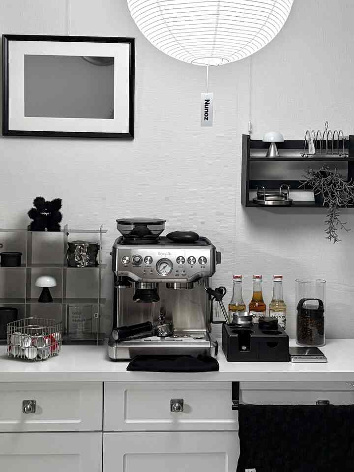 Monotone kitchen space featuring a central espresso machine and pendant light with a clean, cozy home cafe atmosphere