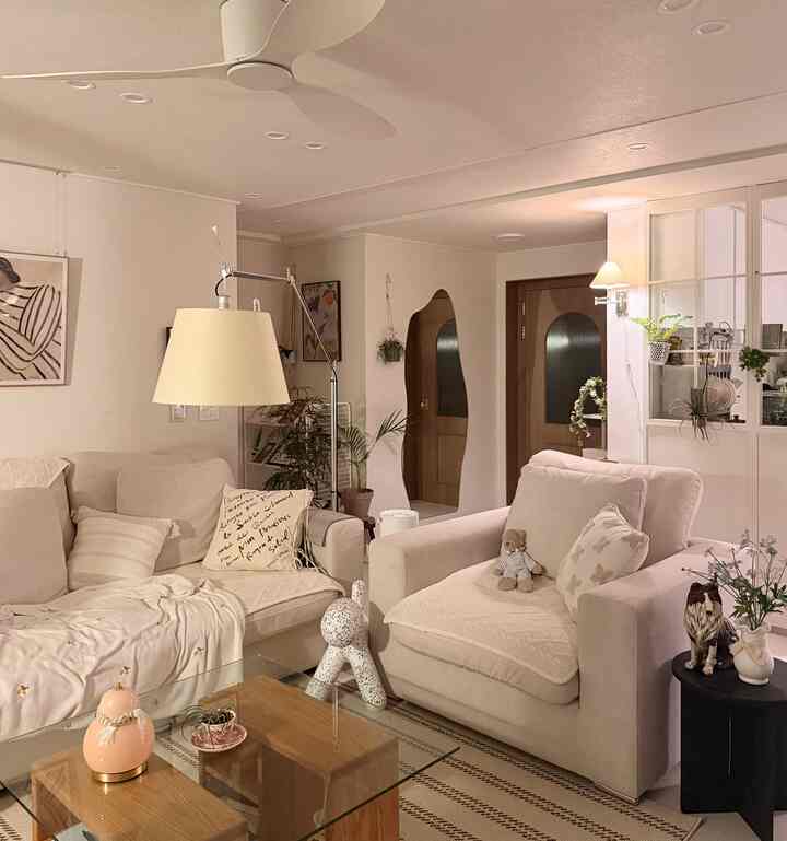 ベージュ調のリビング、ベージュ色のソファとガラスのコーヒーテーブル、壁照明とシーリングファンが調和した雰囲気のある空間