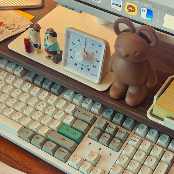 茶色の木製デスクにレトロなキーボードとモニター、かわいいクマとネコのオブジェが配置された雰囲気のあるホームオフィス