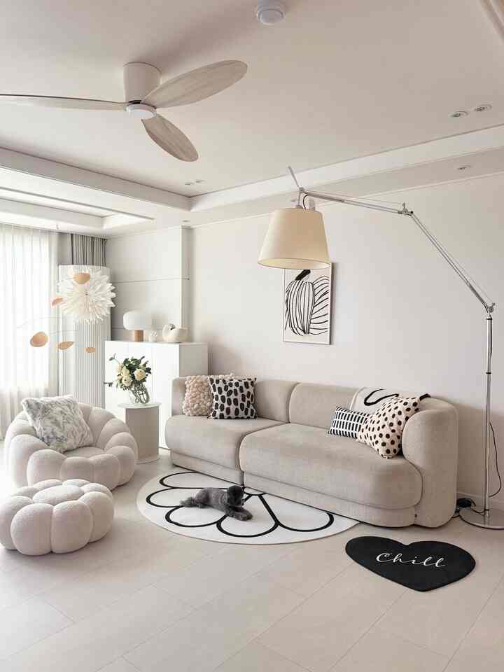 クリームベージュのリビング、曲線のソファとパフアームチェア、フラワーモビールとモダンなフロアランプが配された雰囲気のあるインテリア