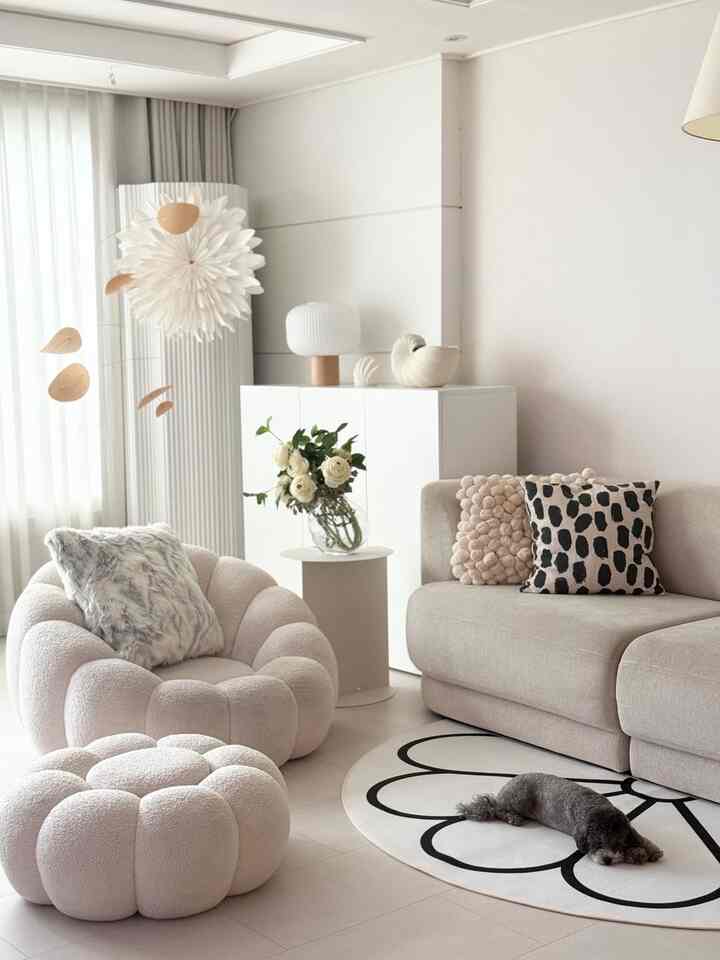 ホワイトとベージュのトーンのリビング、丸いソファとスツール、クッションと花瓶が配置された雰囲気のあるインテリア