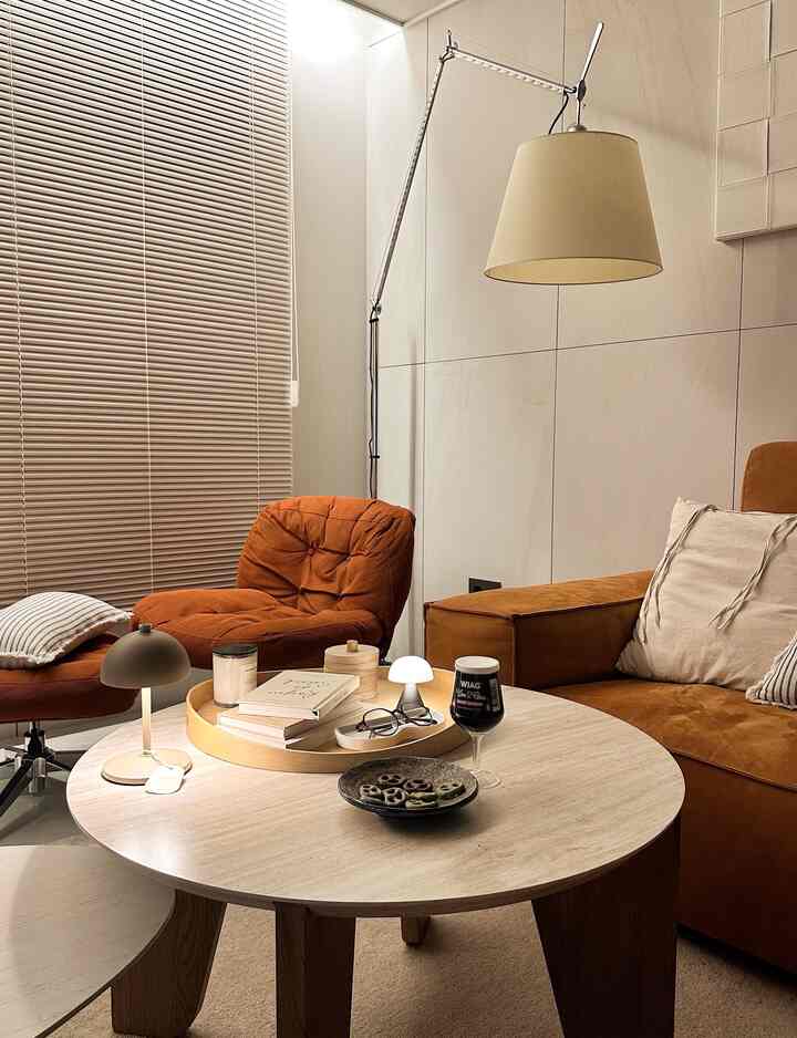 ブラウンとベージュのトーンのリビング、ソファとアームチェアが配置され、丸いコーヒーテーブルに照明と小物が置かれた雰囲気のある空間