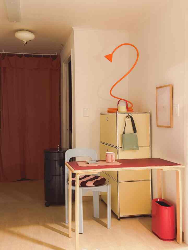 Beige-toned small kitchen space featuring a simple desk, yellow storage cabinet, and an orange lamp creating a cozy ambiance