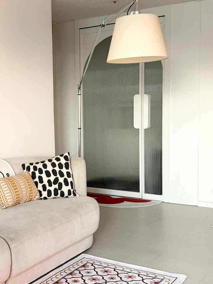 ベージュのソファと白い壁、フロアランプが配置された清潔でモダンなリビングの玄関空間