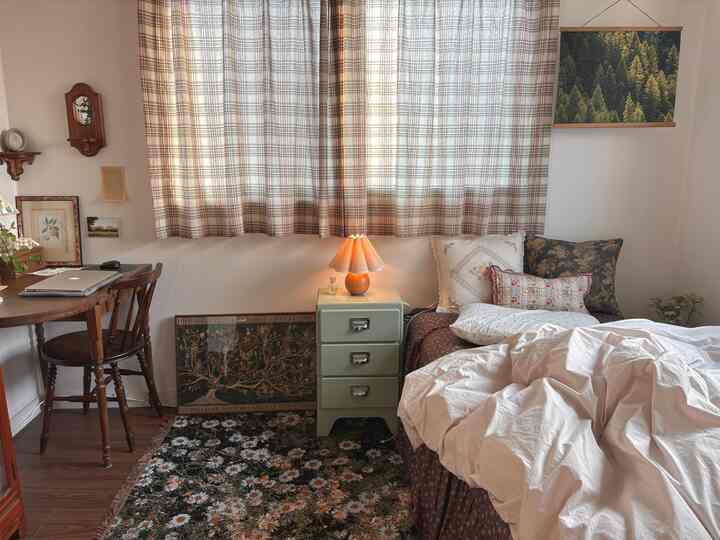 ベージュとブラウンの色調の寝室、木製家具と花柄のラグ、暖かいムード照明が調和したヴィンテージスタイルの印象的な空間