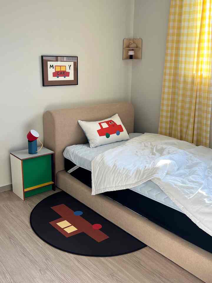 白とベージュのトーンの子供部屋、車のポスターとクッションが配置された明るくシンプルなインテリア