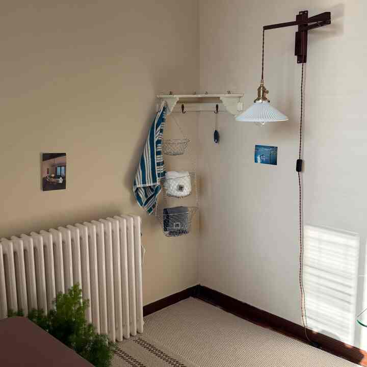 柔らかなベージュの壁とベージュのラグ、モダンな壁灯と収納用の金属バスケットが配置されたコーナースペース