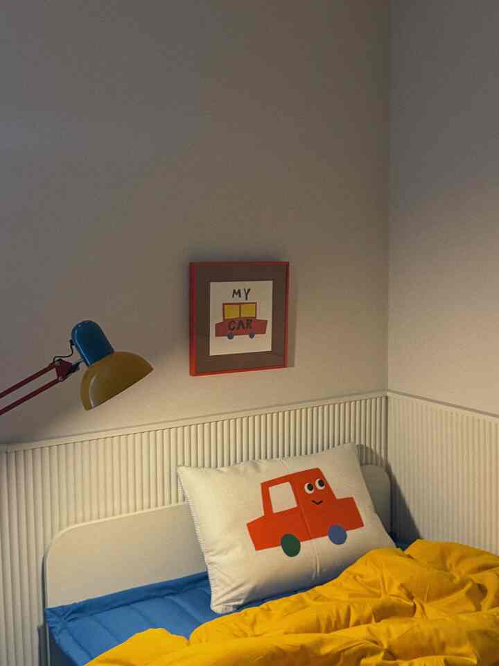 黄色の掛け布団と青いマットレスがある子供部屋、車のモチーフの枕と壁のポスターが配置された温かみのある空間