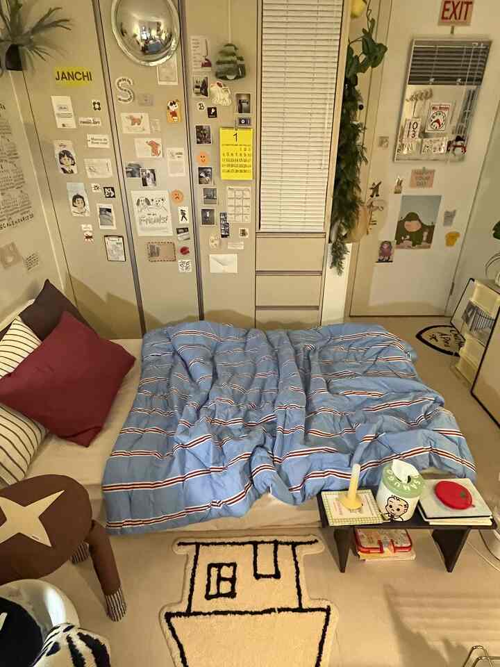 ナチュラルな色調のコンパクトな寝室、青いストライプの布団と壁面収納が配置された落ち着いた空間