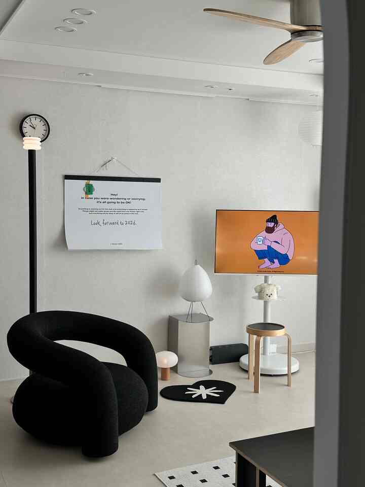 Bright gray toned living room featuring a black curved sofa, round wooden stool, and modern lighting in a simple interior