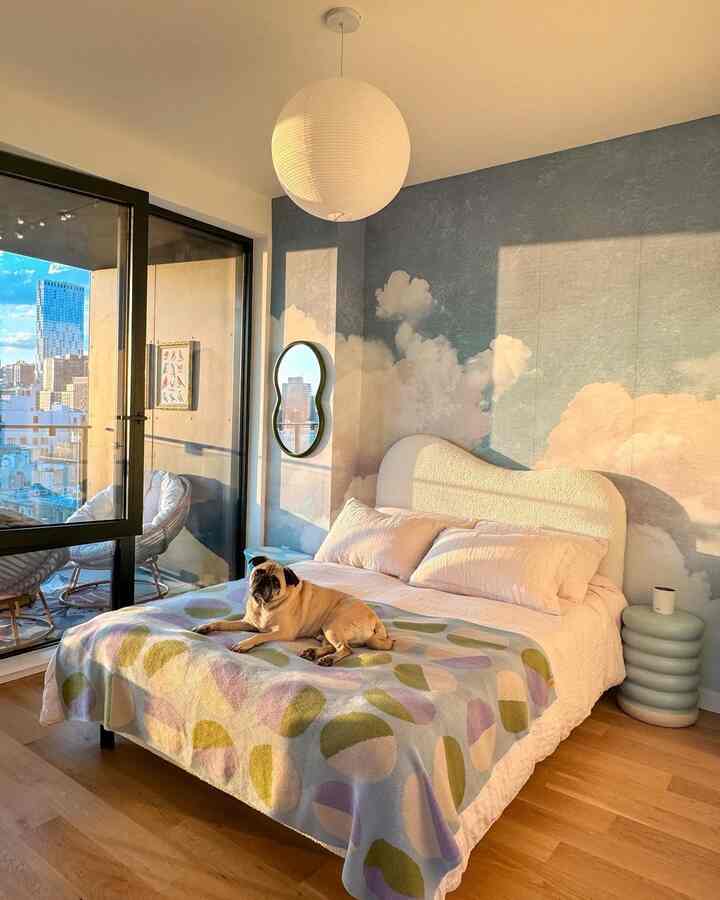 Pastel blue bedroom with cloud mural wall, central bed with a pug dog, creating a cozy atmosphere