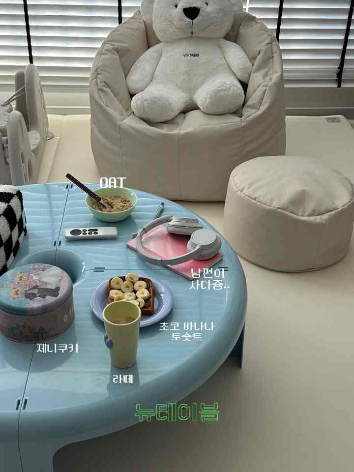 明るいスカイブルーの円形テーブルとベージュのビーンバッグとスツールが配置された、子供と暮らすナチュラルトーンのリビングルーム