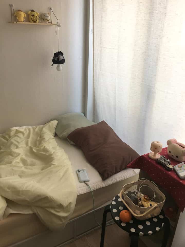 明るいナチュラルカラーの狭い寝室、ベージュのカーテンと寝具、アクセサリーが配置された落ち着いた雰囲気のインテリア