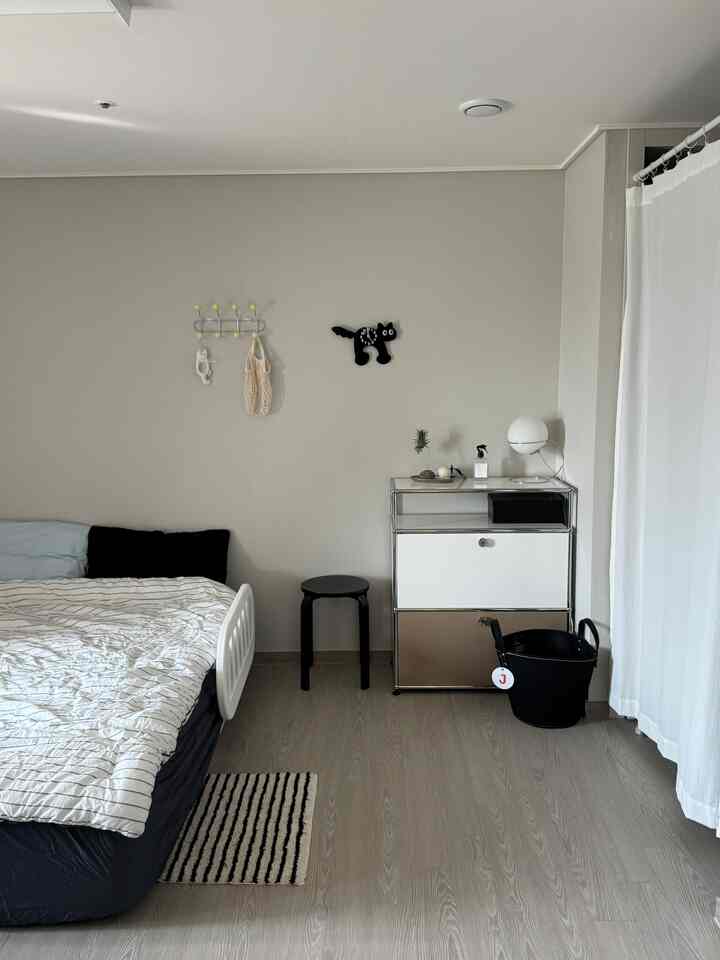 Modern bedroom with white and black tones featuring a bed, stool, and rug in a neat layout