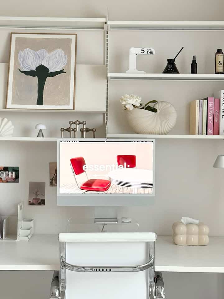 白を基調としたシンプルでモダンなホームオフィス空間。白いデスクとチェア、壁の棚に配置された額縁や小物が印象的です。