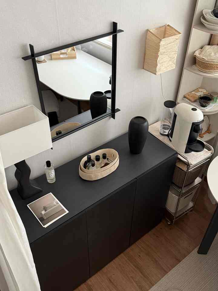 ブラックとナチュラルトーンのリビング、ブラックキャビネットとコーヒーマシン、フロアランプが配置された印象的でミニマルなインテリア