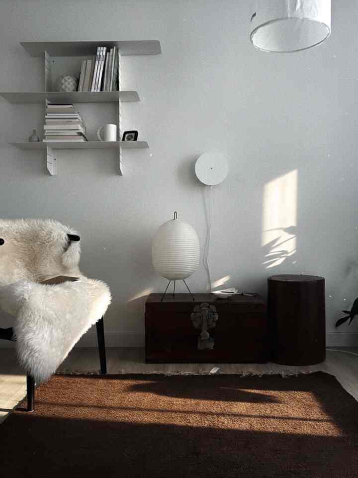 Living room in white and brown tones featuring wall sconces, shelves, and a natural rug with a calm atmosphere