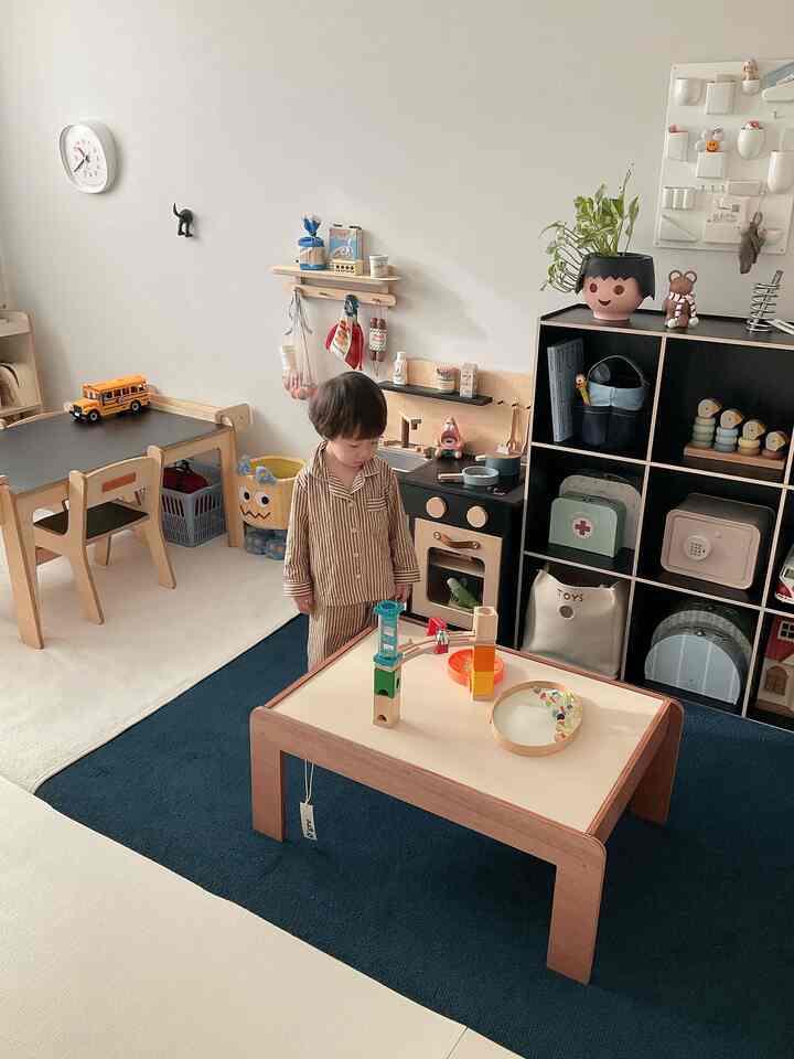 明るいベージュの壁と天然木の家具が調和した子供部屋、小さな木製テーブルで遊ぶ子どもがいる雰囲気のあるインテリア