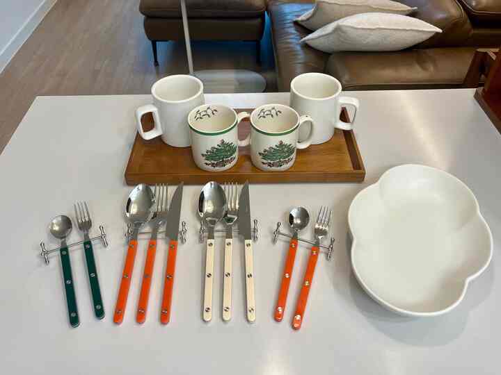 ホワイトトーンのキッチンには、カラフルなカトラリーとヴィンテージ風のクリスマスマグカップ、雲型のオーバルボウルが配置された清潔感のある空間