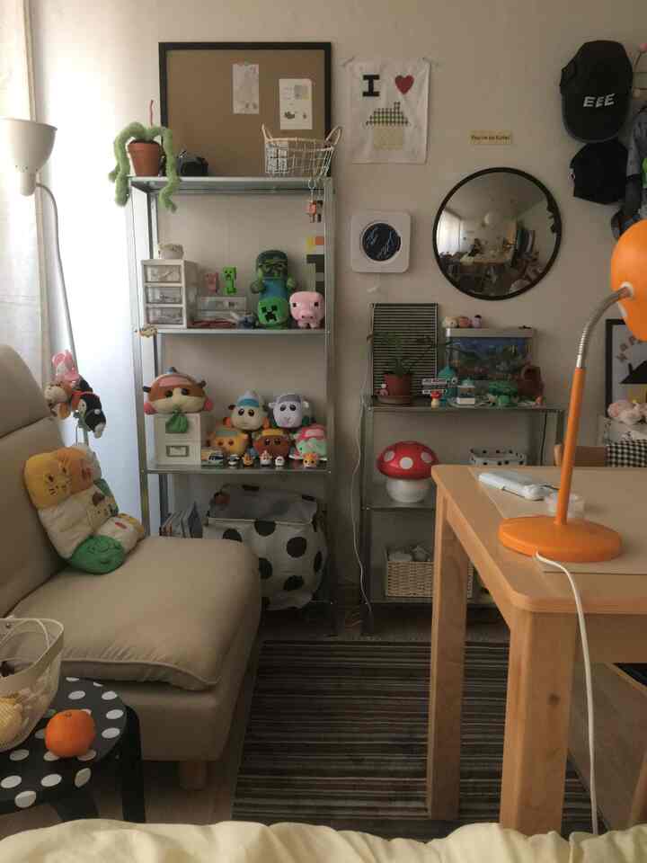 ベージュのソファと木製テーブルがある小さな部屋、棚や額縁、かわいらしい小物が配置された雰囲気のあるインテリア