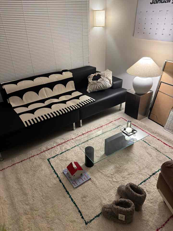 黒いソファと白いラグが配置されたリビング、柄入りのブランケットとテーブルランプが調和した落ち着いた空間